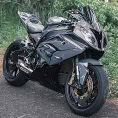 a black motorcycle parked on the side of a road next to some grass and bushes