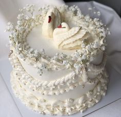 two white swans on top of a wedding cake decorated with flowers and pearls, sitting in the middle of a circle