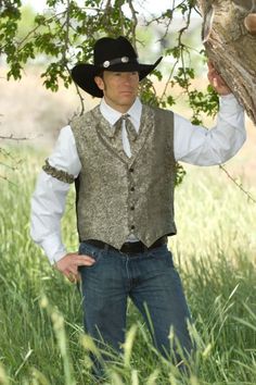 a man wearing a cowboy hat and vest standing in tall grass