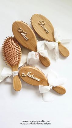 three personalized wooden hairbrushes with white bows and name on the brushes are laying next to each other