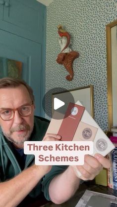 a man sitting at a table holding up two kitchen schems in front of him