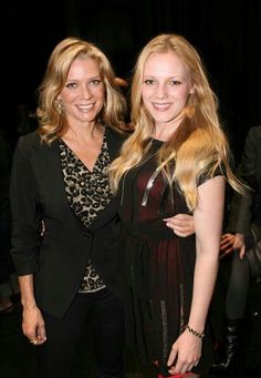 two beautiful women standing next to each other in front of a black background and one is holding a red purse