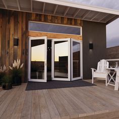 an open patio door on a deck with white chairs and potted plants next to it