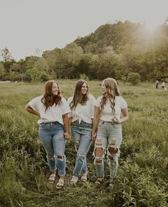 three girls standing in the grass with their arms around each other and looking at something