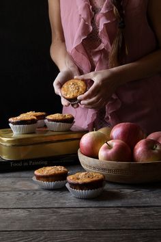 a woman in pink is holding a pie and some apples on a table with other food