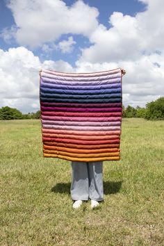 a person holding up a multicolored blanket in the grass