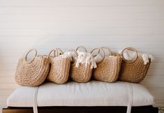 six straw bags sitting on top of a white bench in front of a wooden wall