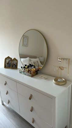 a white dresser with a round mirror on top and other items sitting on the drawers