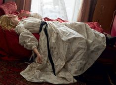 a woman laying on top of a red bed in a room next to a window