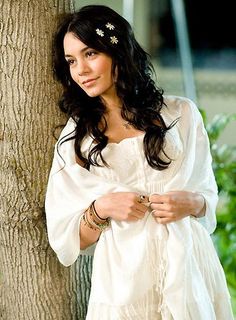 a woman standing next to a tree wearing a white shirt and flowered hair clip