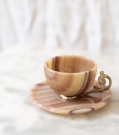 a small wooden cup and saucer on a marble plate with a gold metal handle