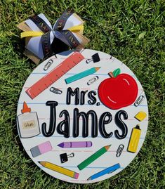 a teacher's ornament with an apple and school supplies on it, sitting in the grass