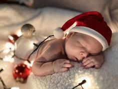 a baby wearing a santa hat laying on top of a bed next to christmas decorations