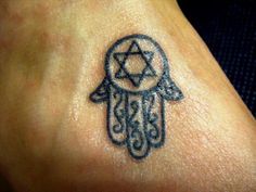 a small hamsa tattoo on the foot of a person's left foot, with a star of david in the middle