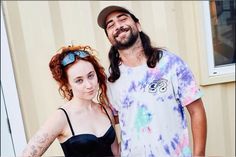 a man and woman standing next to each other in front of a building with a tie dye shirt on