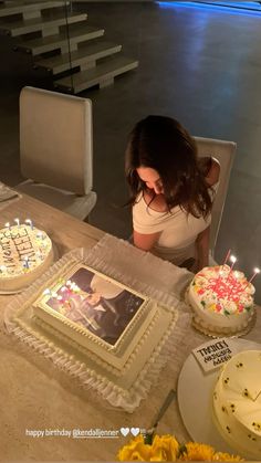 a woman sitting at a table with two cakes and candles in front of her,