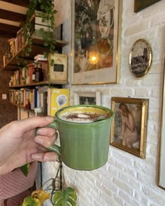 a person holding a cup of coffee in front of a wall with pictures on it