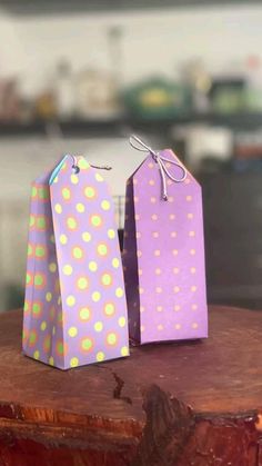 two small purple and yellow gift bags sitting on top of a wooden stump in a kitchen