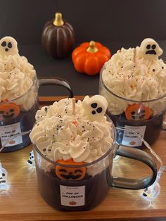 three halloween desserts in plastic cups on a wooden table with pumpkins behind them