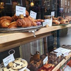 there are many pastries on display in the store window and behind them is an assortment of croissants