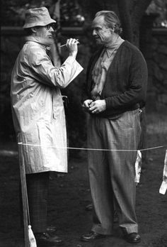 two men standing next to each other on a dirt ground with clothes hanging up in the air