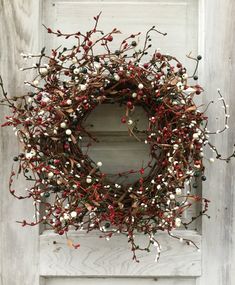 a wreath is hanging on the side of a door with red berries and white flowers