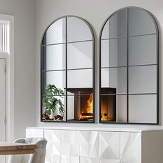 two arched windows with a fireplace in the middle and a potted plant behind them