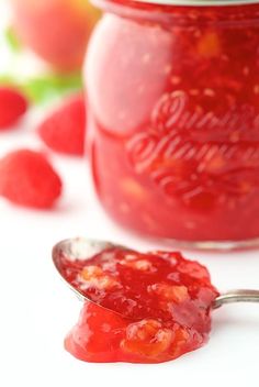 a spoon full of raspberry jam next to a jar filled with raspberries