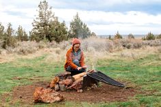 a woman sitting on top of a tree stump next to a campfire with an open grill