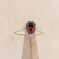 a close up of a ring on top of a wooden stand with a red stone in the center