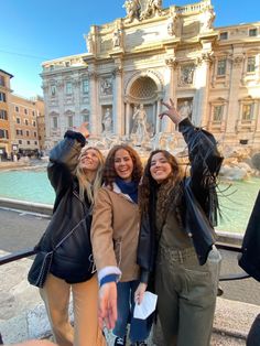 three young women standing next to each other in front of a fountain with their arms up