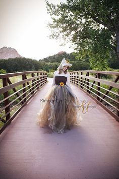 a woman is walking across a bridge wearing a dress and hat with flowers on it