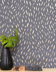 a black vase sitting on top of a wooden table next to a wallpaper covered in white dots