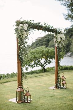 an outdoor ceremony setup with lanterns, flowers and greenery on the grass by the water