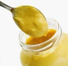 a spoon full of yellow liquid is being held up by a glass jar filled with it