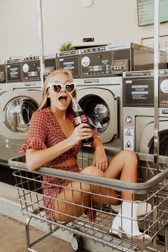 a woman sitting in a laundry basket with a bottle of soda next to washing machines