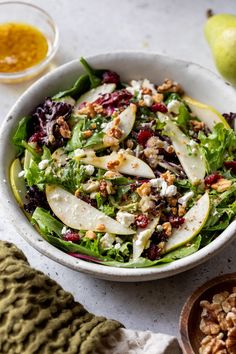 a salad with apples, cranberries and walnuts in a white bowl on a table