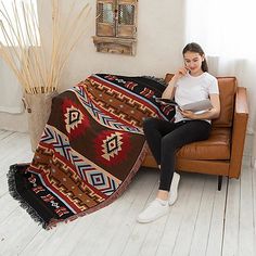 a woman sitting on a couch with a laptop and blanket in front of her, while talking on the phone