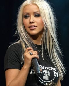 a woman with long blonde hair and piercings holding a microphone in her right hand