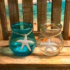 two glass vases sitting on top of a wooden table next to each other with starfish charms hanging from them