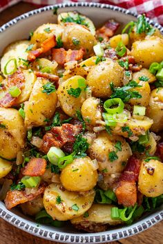 a bowl filled with potatoes and bacon on top of a wooden table next to a red checkered napkin