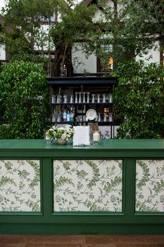 a green and white bar sitting in front of a building with lots of greenery