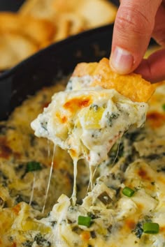 a hand holding a tortilla chip over a skillet filled with cheese and spinach dip