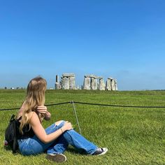 a woman sitting on the grass in front of stonehenge