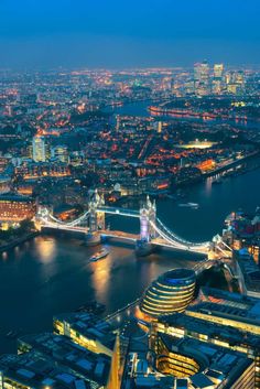 an aerial view of london at night with the tower bridge in the foreground and city lights lit up