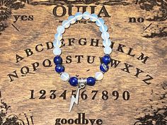 a blue beaded bracelet with white beads and a silver cross on it, sitting on top of a wooden plaque