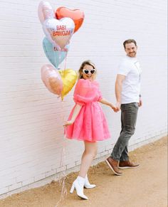 a man and woman holding hands while standing in front of a brick wall with balloons