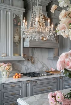 a chandelier hanging from the ceiling in a kitchen with gray cabinets and marble counter tops