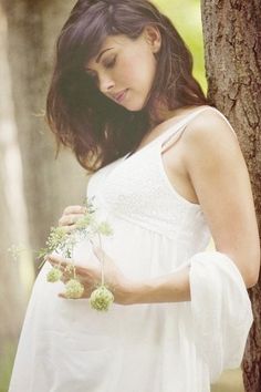 a pregnant woman standing next to a tree