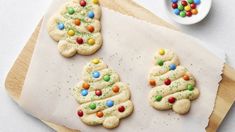 three decorated cookies on a cutting board next to a bowl of candy